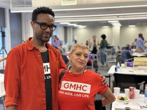 GMHC staff Armstrong Tingwane and Lillibeth Gonzalez pose in black and red GMHC t-shirts respectively.