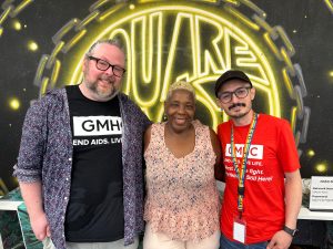 Three GMHC staff members, Chris, Ms. Victoria, and Daniel, in front of a neon mural.